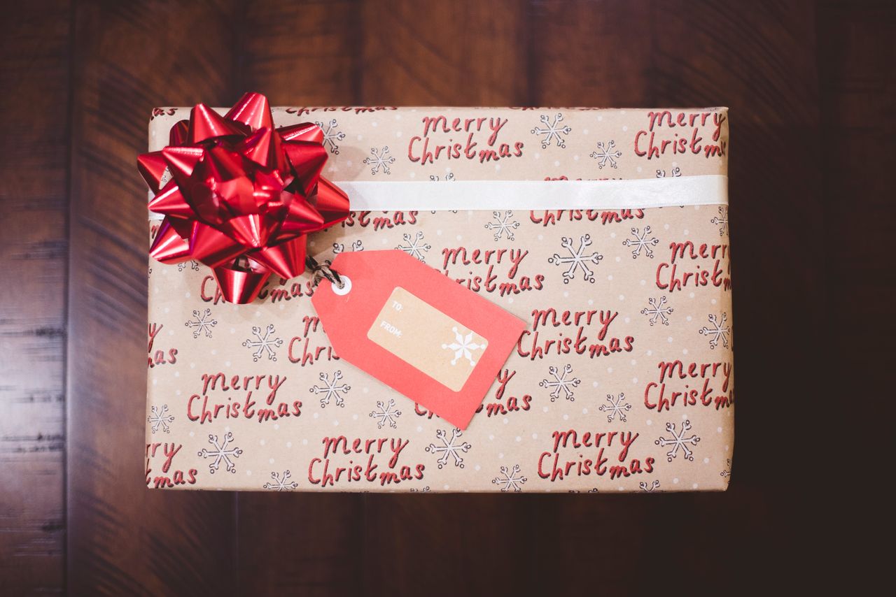 A Christmas gift wrapped in festive paper with "Merry Christmas" written in red, adorned with a large red bow and a gift tag.