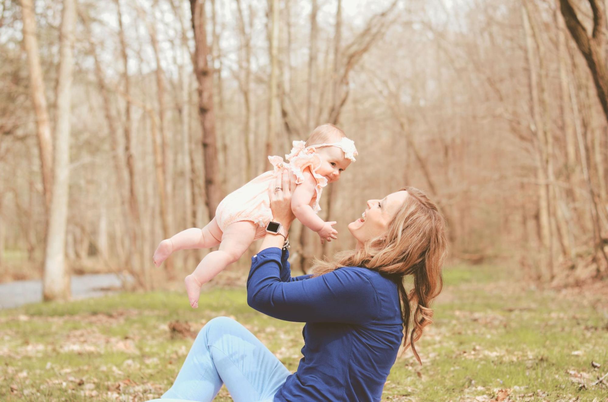 A woman in dark blue longsleeve sits in the park and holds her baby girl