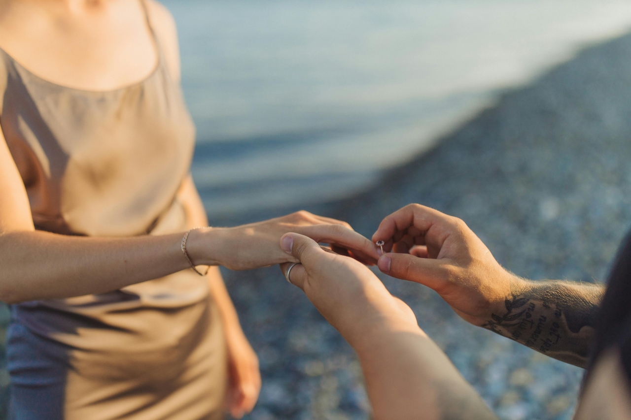 A man putting a custom engagement ring on his lady’s finger for a special sunset Valentine’s Day proposal