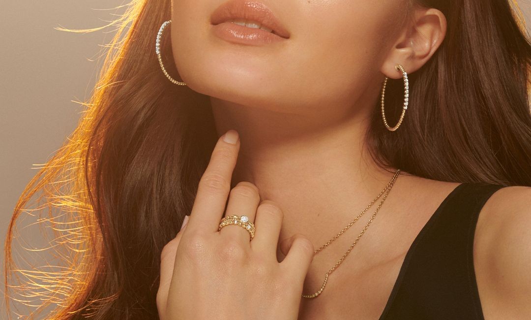 A stylish woman wearing large diamond and gold hoop earrings, layered gold necklaces, and stacked gold rings with diamonds.