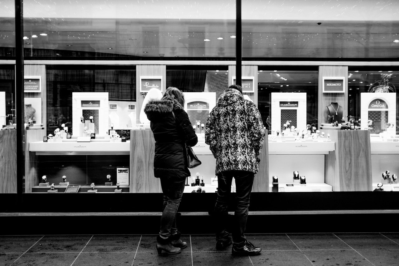 Black and white photo of two people in winter coats looking at a jewelry store display.
