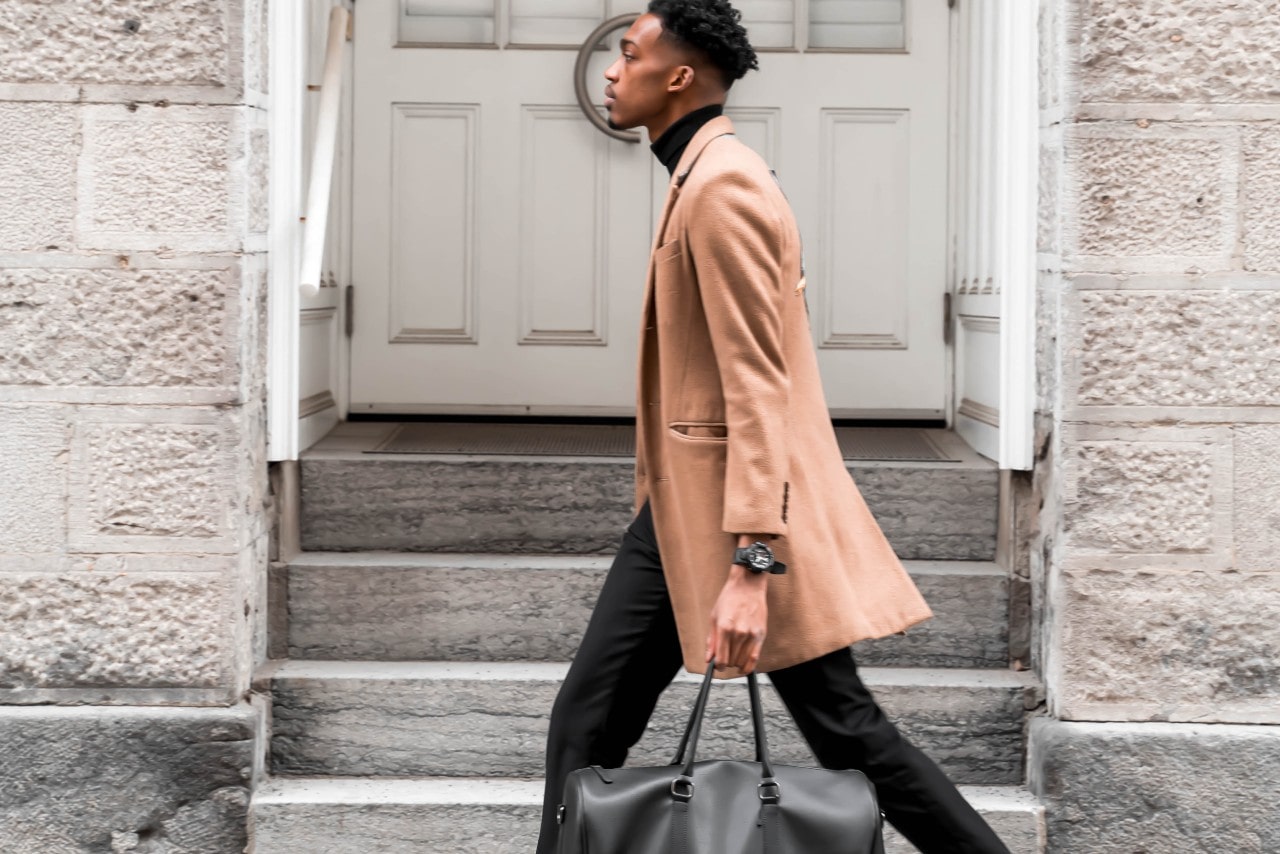 a man in a brown coat walking down the street wearing a black watch