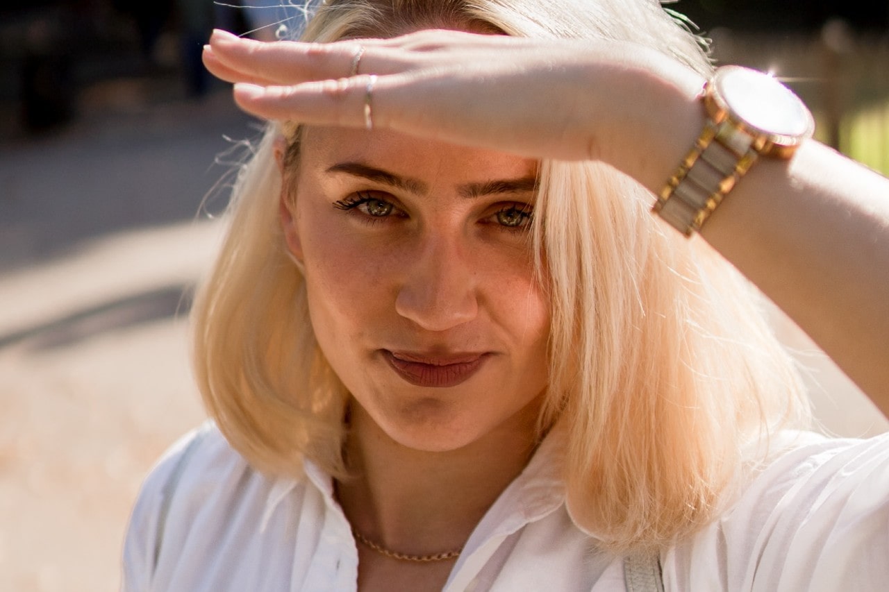 a woman shading her eyes from the sun, wearing a mixed metal watch