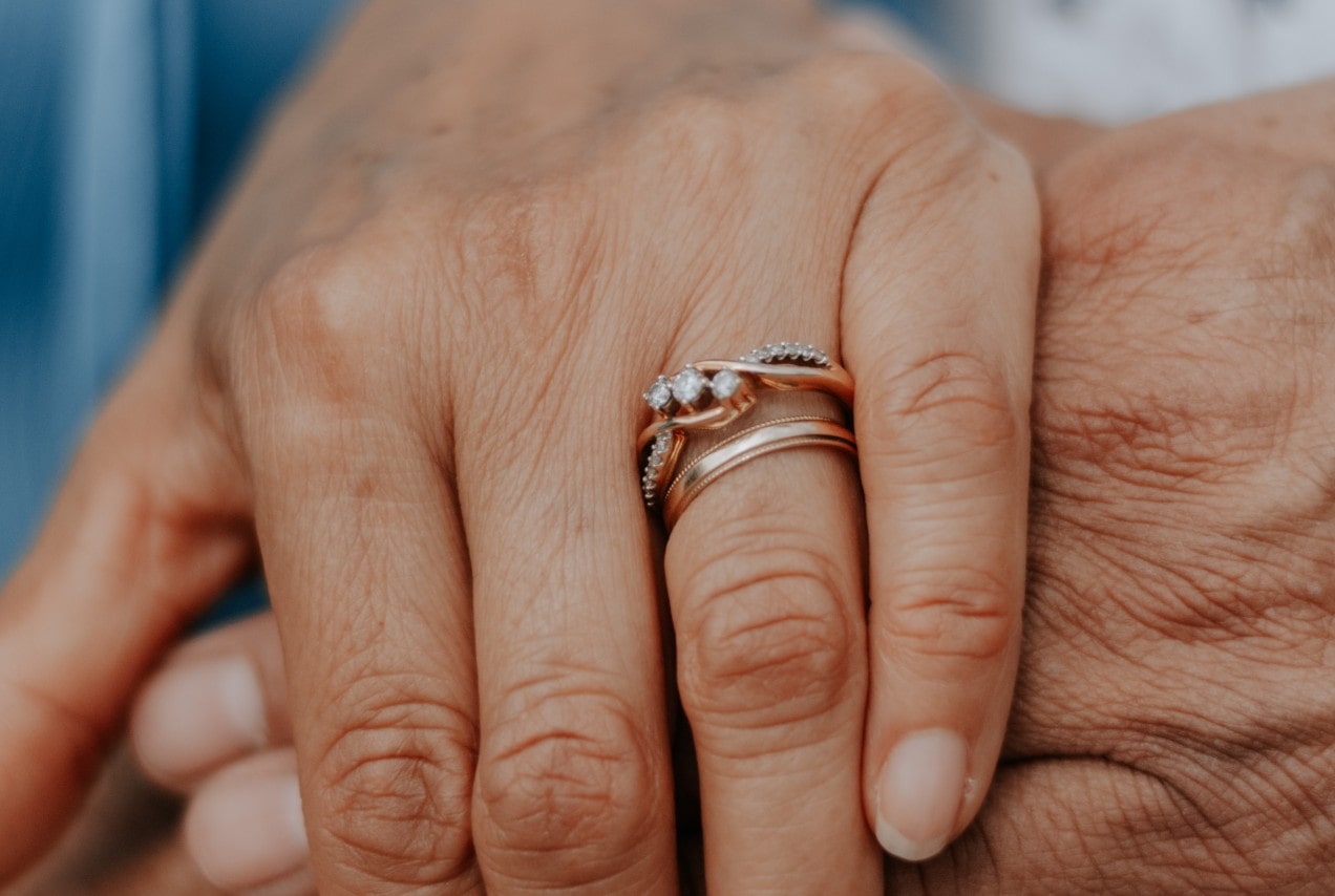 a hand wearing two bridal rings is clasping another hand