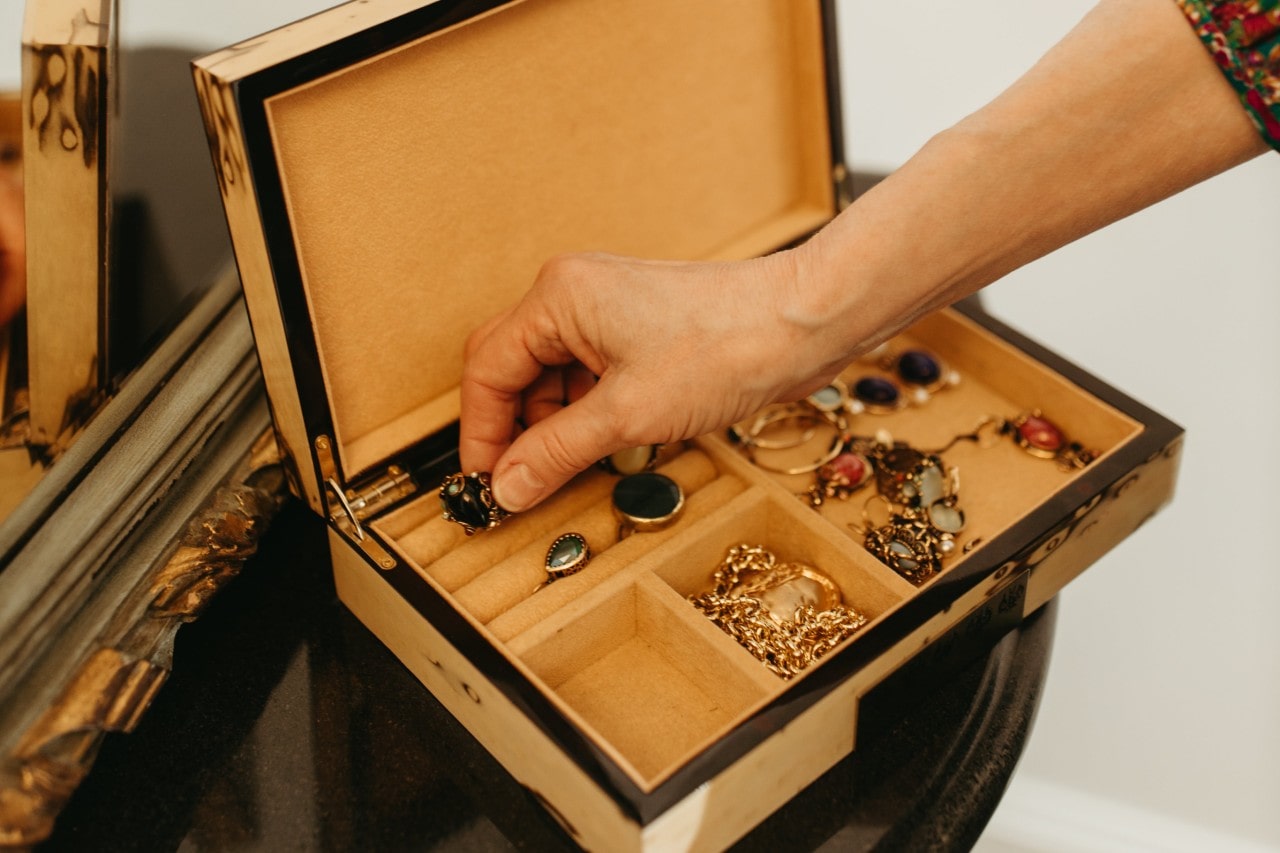 A person putting an antique broach in a jewelry box filled with other vintage jewelry.