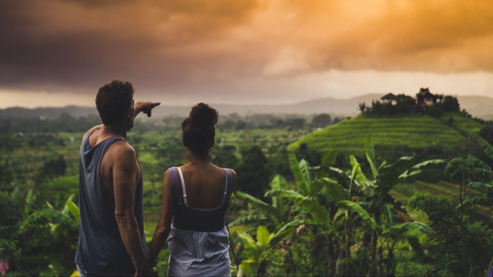 A couple overlooking a beautiful tropical scenery, the man pointing to a large mountain in the distance.