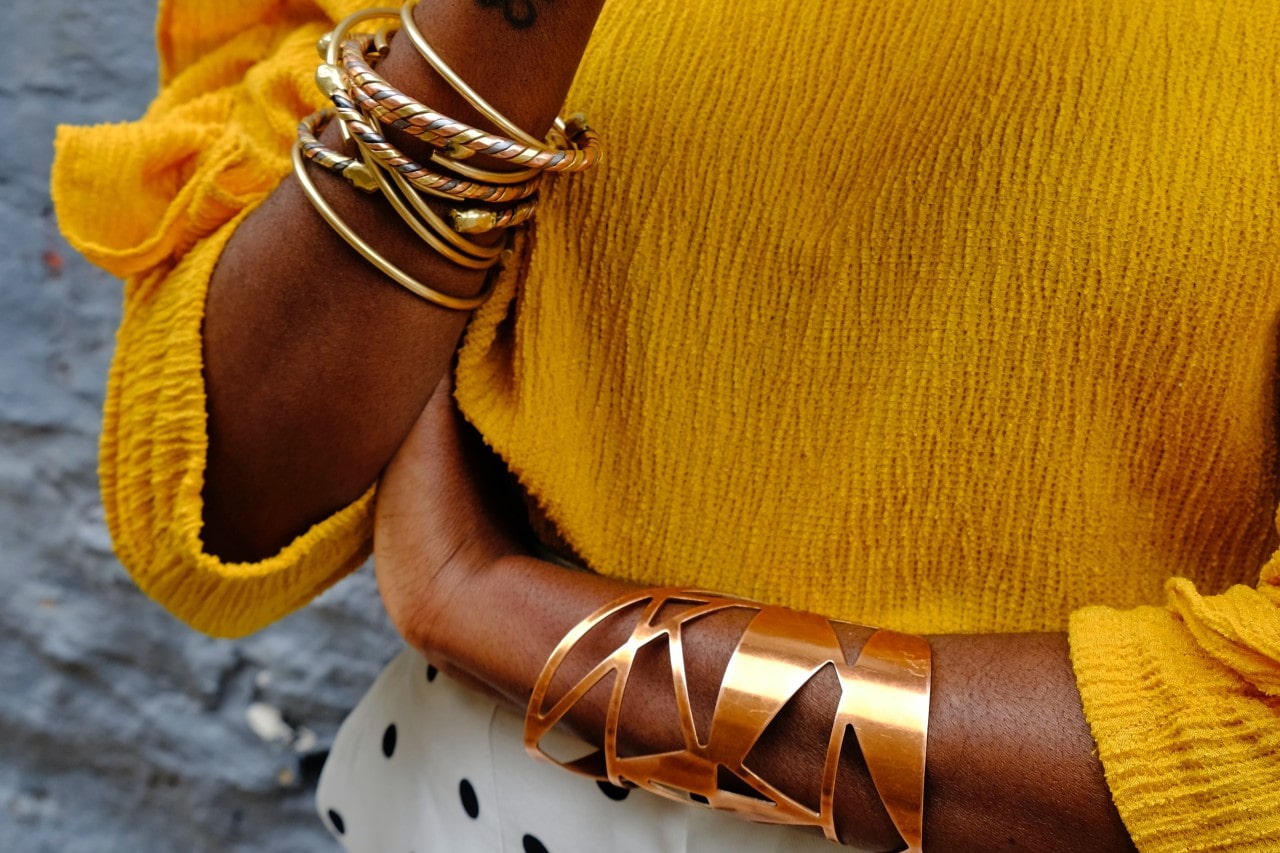 A close-up of a person in a yellow blouse with multiple yellow gold bangles on their hands.