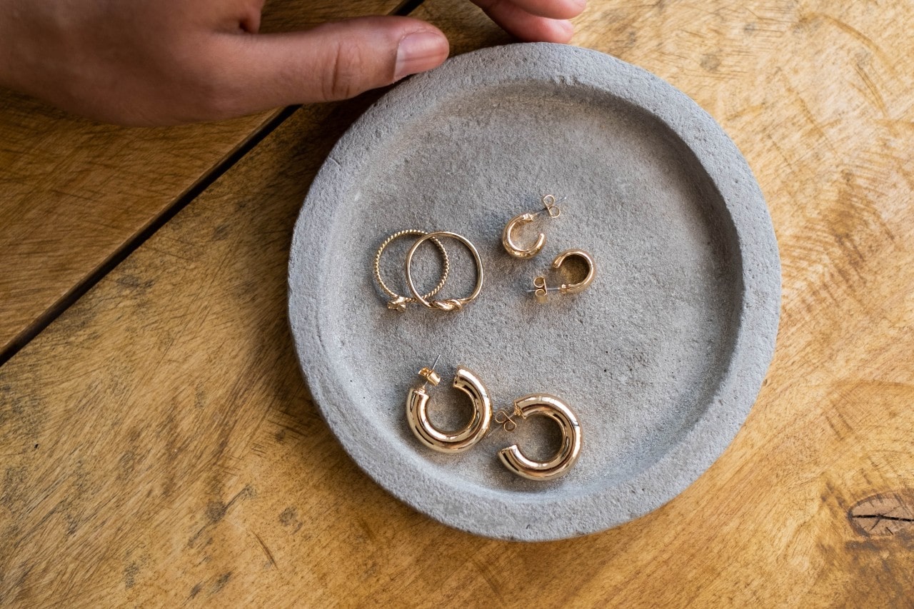 Several yellow gold huggie earrings on a round grey jewelry plate, sat on top of a wooden surface.