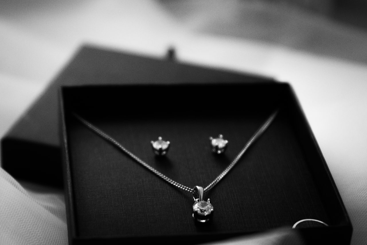 A black and white close-up of a matching jewelry set featuring a diamond pendant necklace and stud earrings