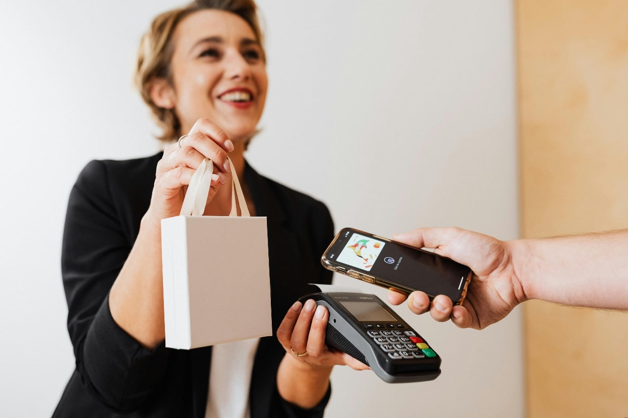A view of a jeweler happily handing a customer their purchase as they pay with their phone.