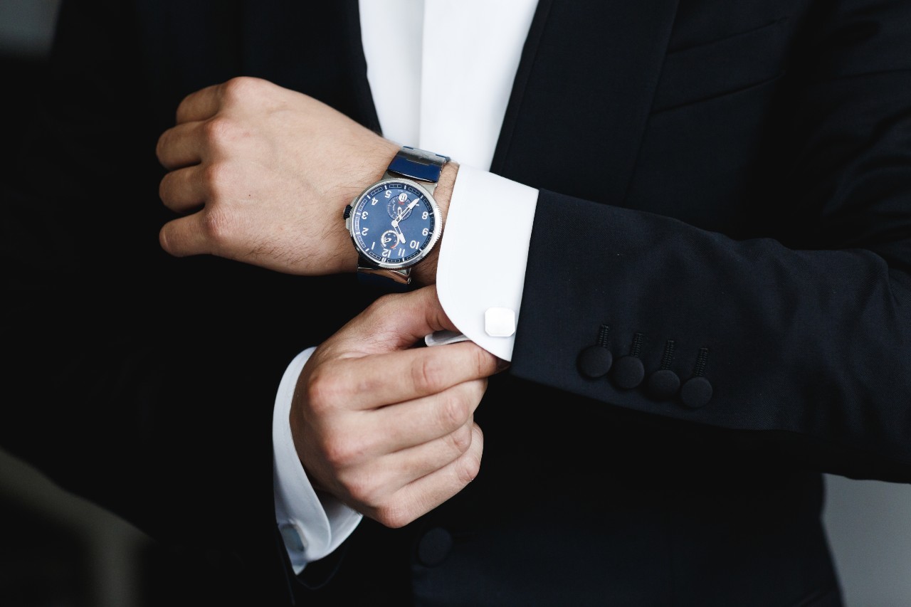 Man in a suit fastening his cufflinks, with his watch clearly visible