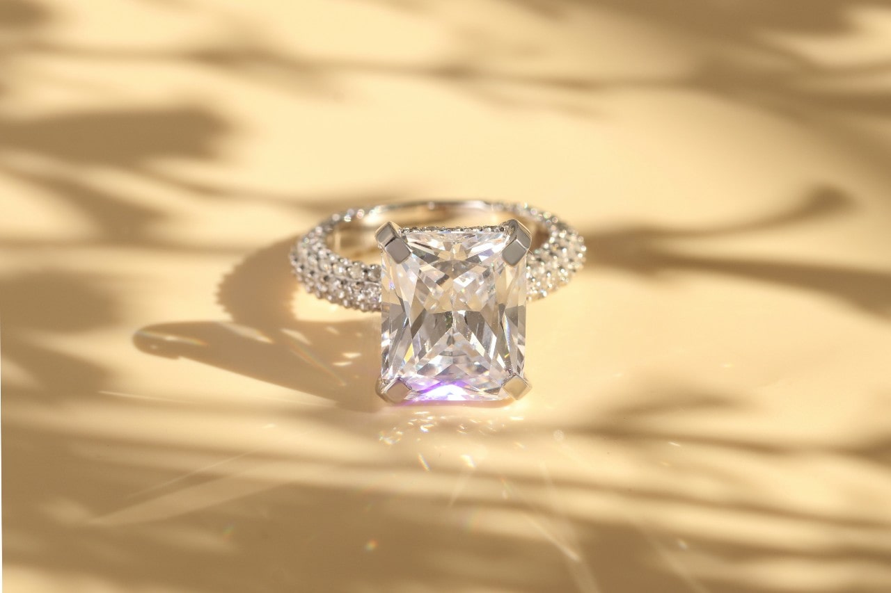 A silver, emerald cut engagement ring with side stones on a yellowish surface