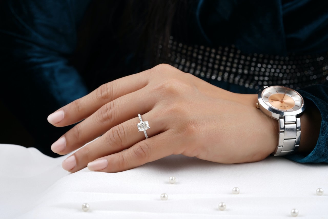 A hand resting on a white surface, wearing a silver, emerald cut engagement ring with side stones