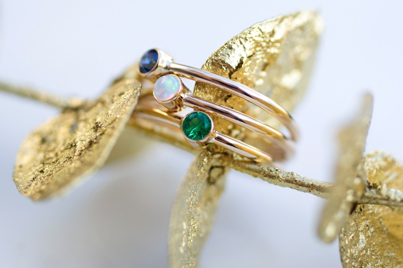 A beautiful stackable ring with blue, opal, and green gemstones rest on golden leaves.