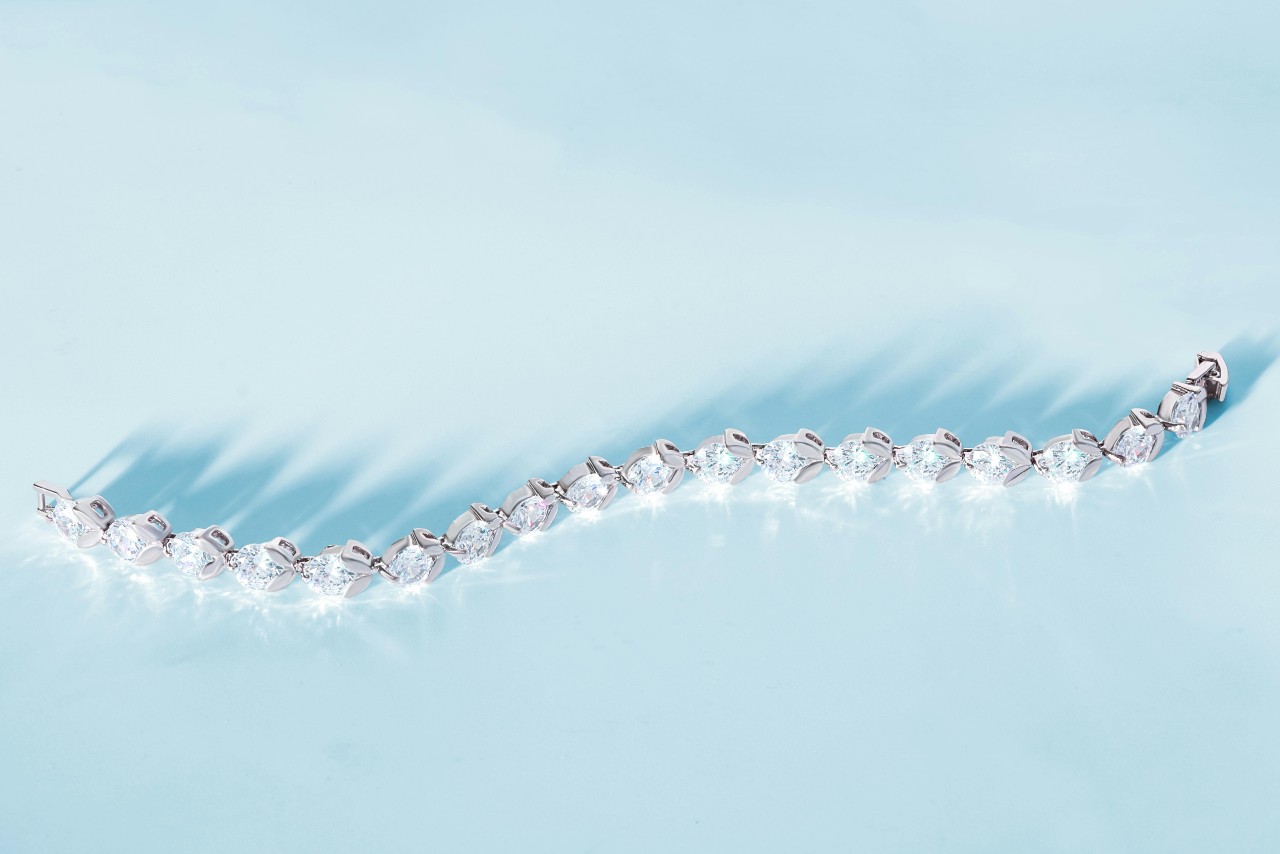 A top-down view of a dazzling diamond tennis bracelet displayed on a pale blue background. A top-down view of a dazzling diamond tennis bracelet displayed on a pale blue background.