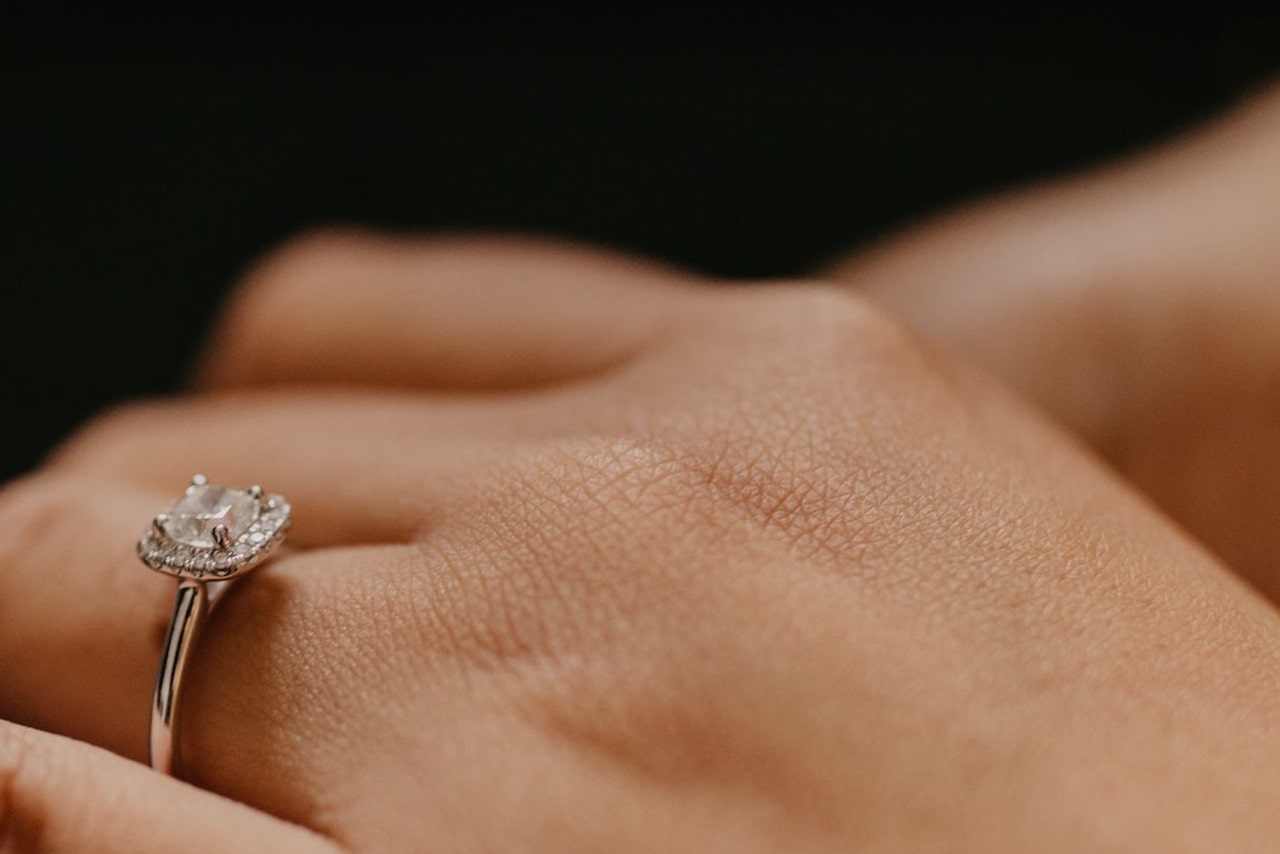 Close up image of a halo set, princess cut engagement ring on someone’s finger