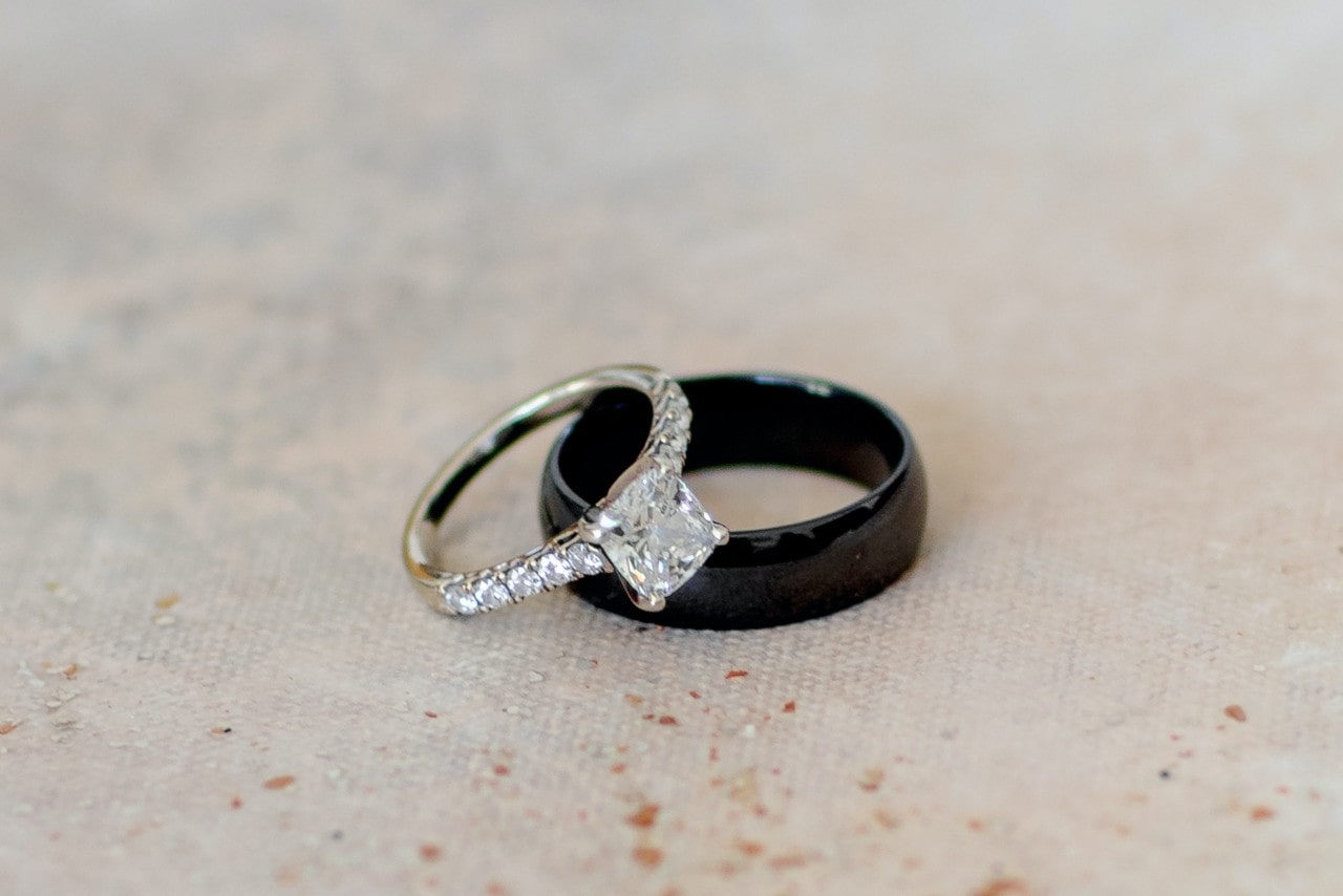 A side stone princess cut engagement ring lying on a black wedding band