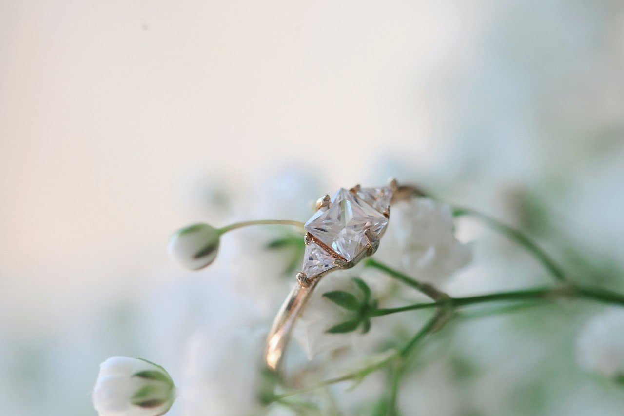 A princess cut, three stone engagement ring surrounded by flowers