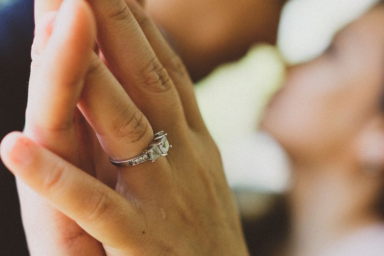 Close up of hands pressed together, one wearing a side stone engagement ring