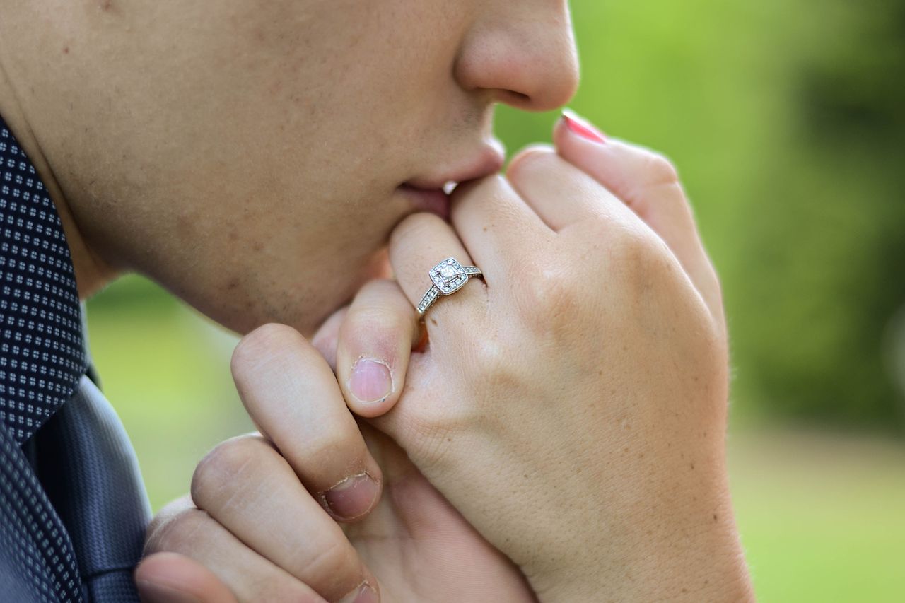 Man kissing a woman’s hand while she wears a side stone engagement ring