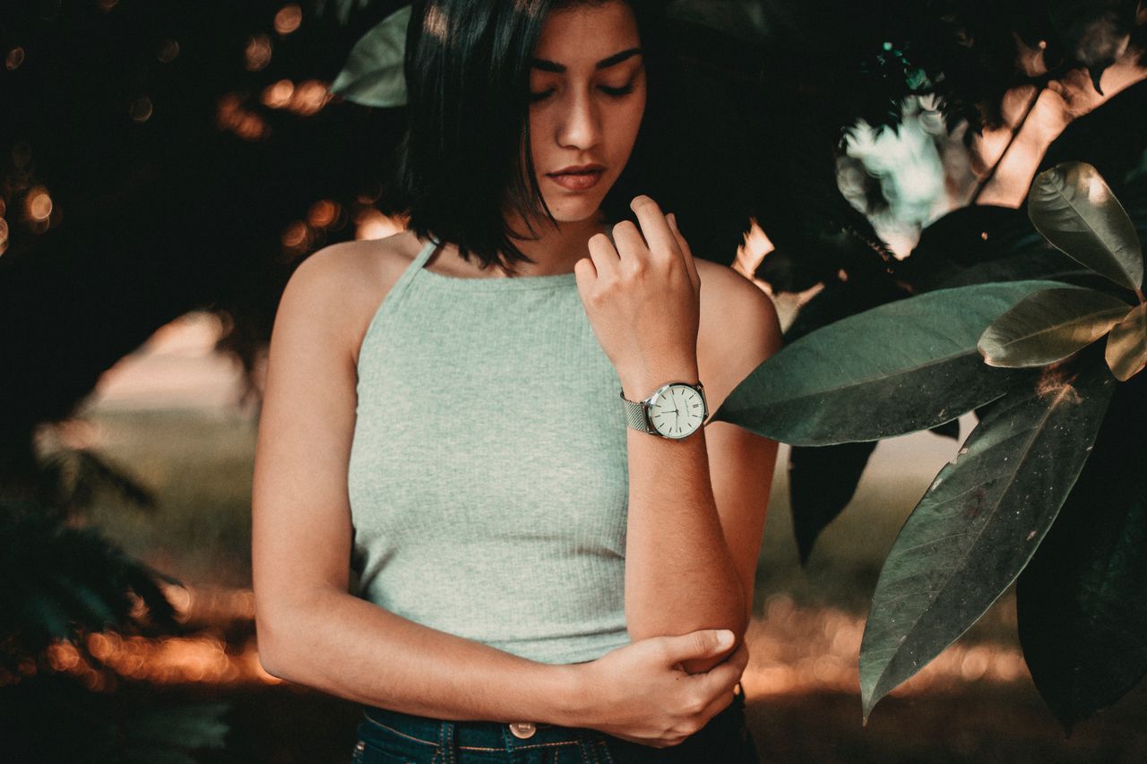 A wide angle shot of a young woman wearing a luxury watch standing among leafy trees. A wide angle shot of a young woman wearing a luxury watch standing among leafy trees.