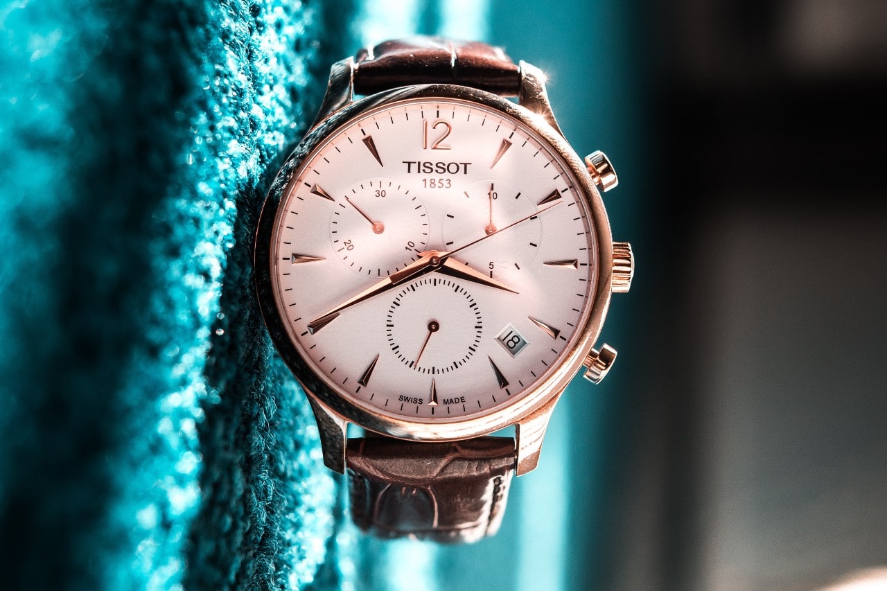 A close-up of a Tissot watch resting on a soft teal surface, rotated to make the watch appear as if it’s floating. A close-up of a Tissot watch resting on a soft teal surface, rotated to make the watch appear as if it’s floating.