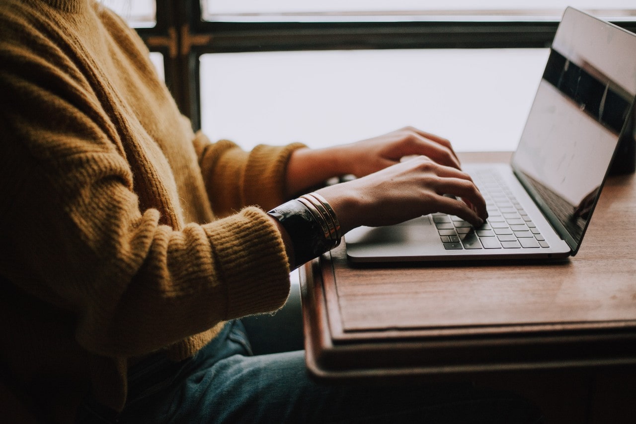 A person typing on a laptop and wearing a number of large bracelets