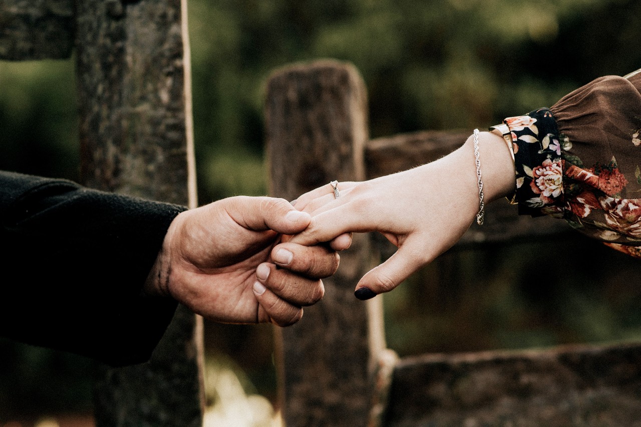 A couple holds hands, the woman wearing a white gold engagement ring.