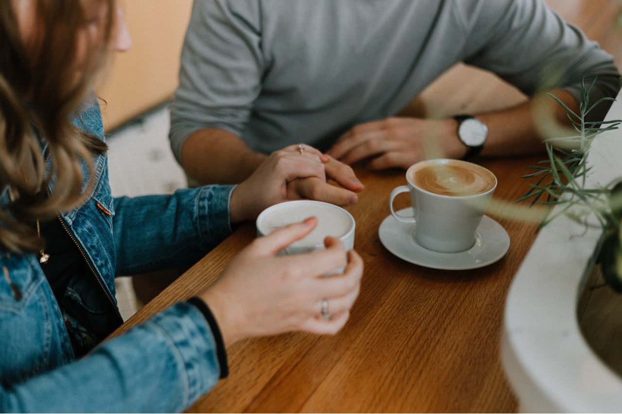 An engaged couple sips coffee in a cafe while talking.