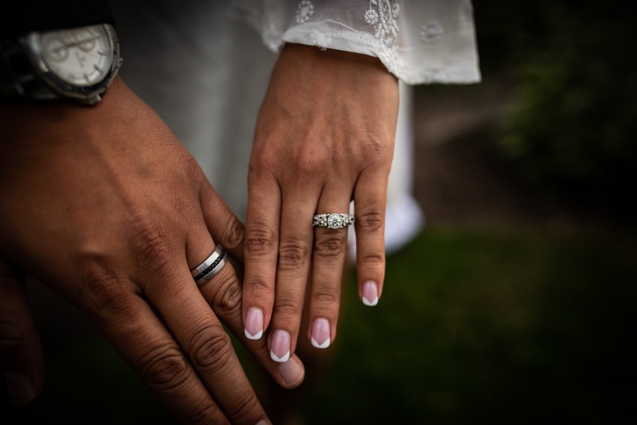 A bride and groom show off their engagement ring and wedding band.