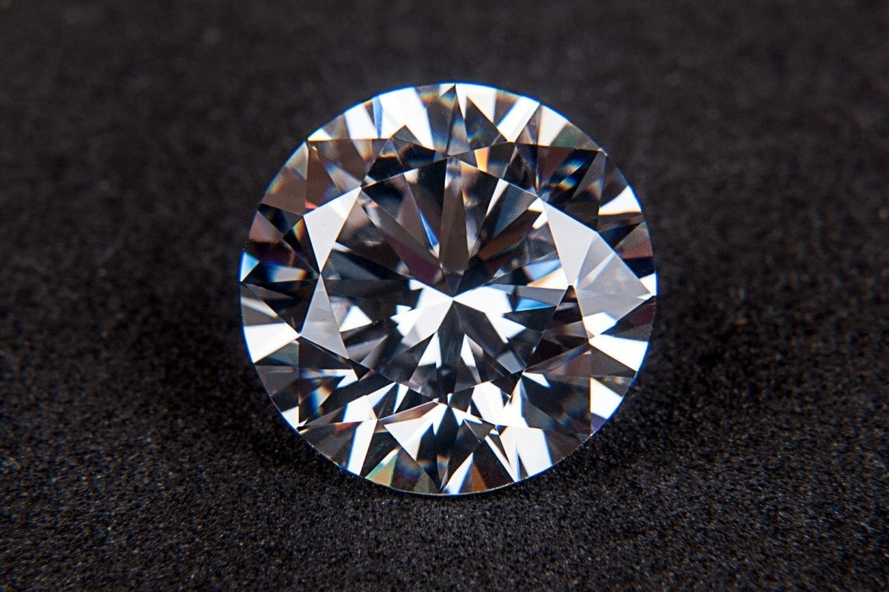 A close-up of a dazzling round cut diamond on a soft grey background.