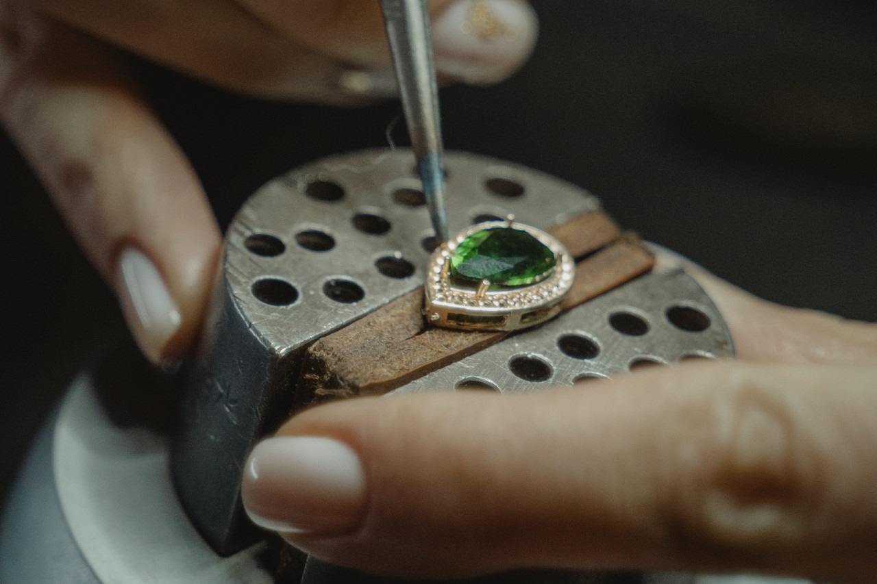 A close-up of a jeweler making a custom engagement ring with a pear cut emerald. A close-up of a jeweler making a custom engagement ring with a pear cut emerald.